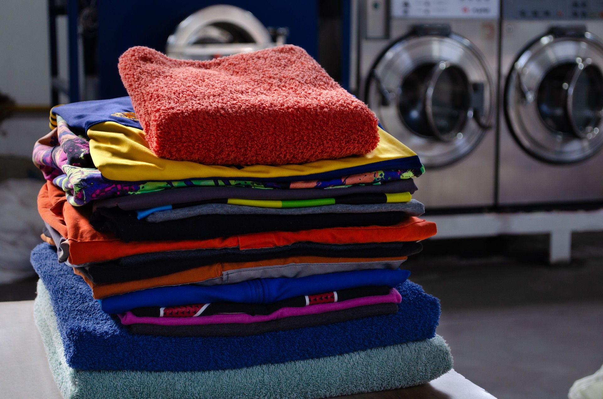 Stack of colorful cotton clothes in an industrial laundry with washing machines behind. Stack of colorful cotton clothes in an industrial laundry with washing machines behind.